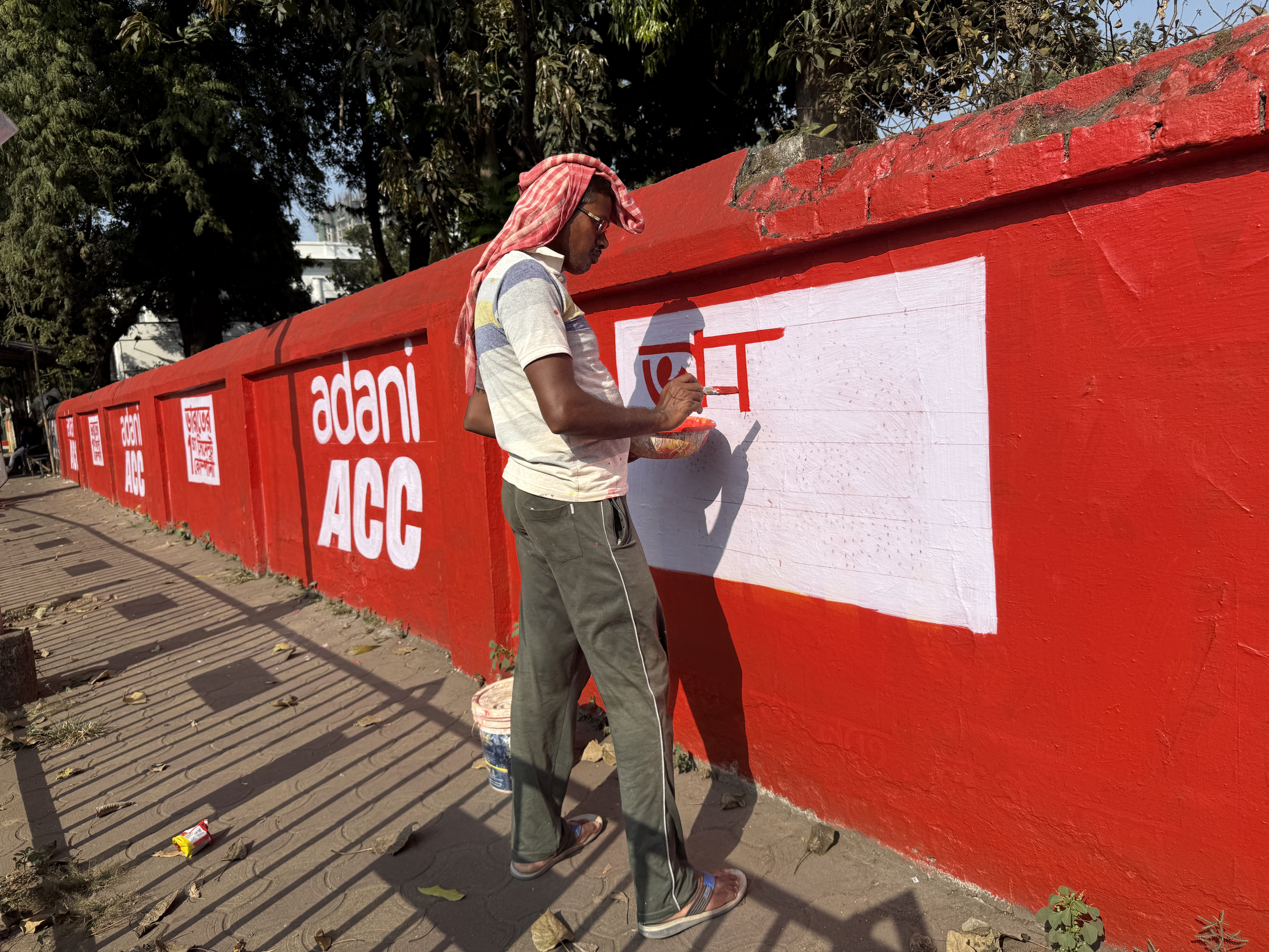 On-ground brand activation — a trained field worker painting the Adani ACC brand wall across a street in India, demonstrating the invisible labour behind BTL marketing